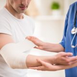 At doctor's Close-up of female doctor with stethoscope bandaging hand of male patient.