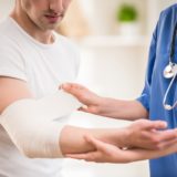 Close-up of female doctor with stethoscope  bandaging hand of male patient.