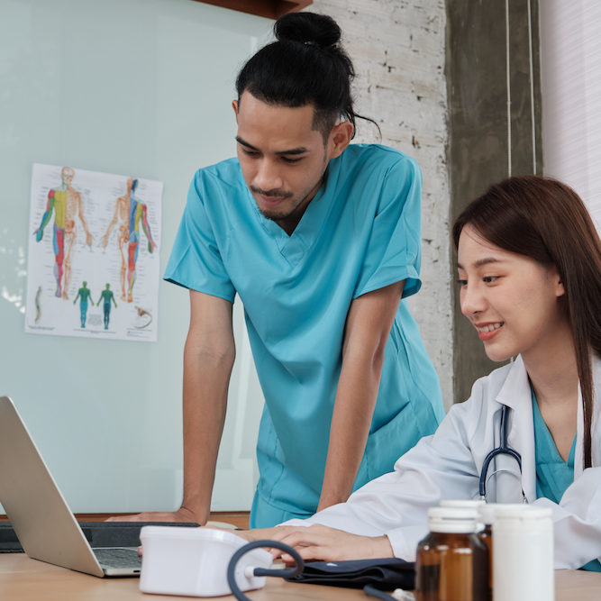 Healthcare team partners. Two uniformed young Asian ethnicity doctors are co-workers discussing medication in hospital's clinic office. Specialist persons are experts and professionals.